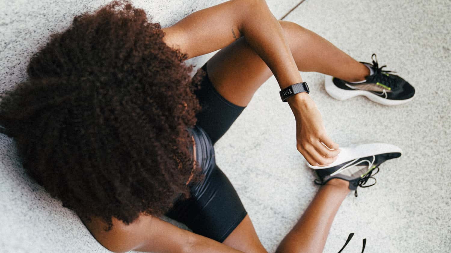 上方照片显示,一位穿运动服的黑人妇女望手腕上的健康监视器